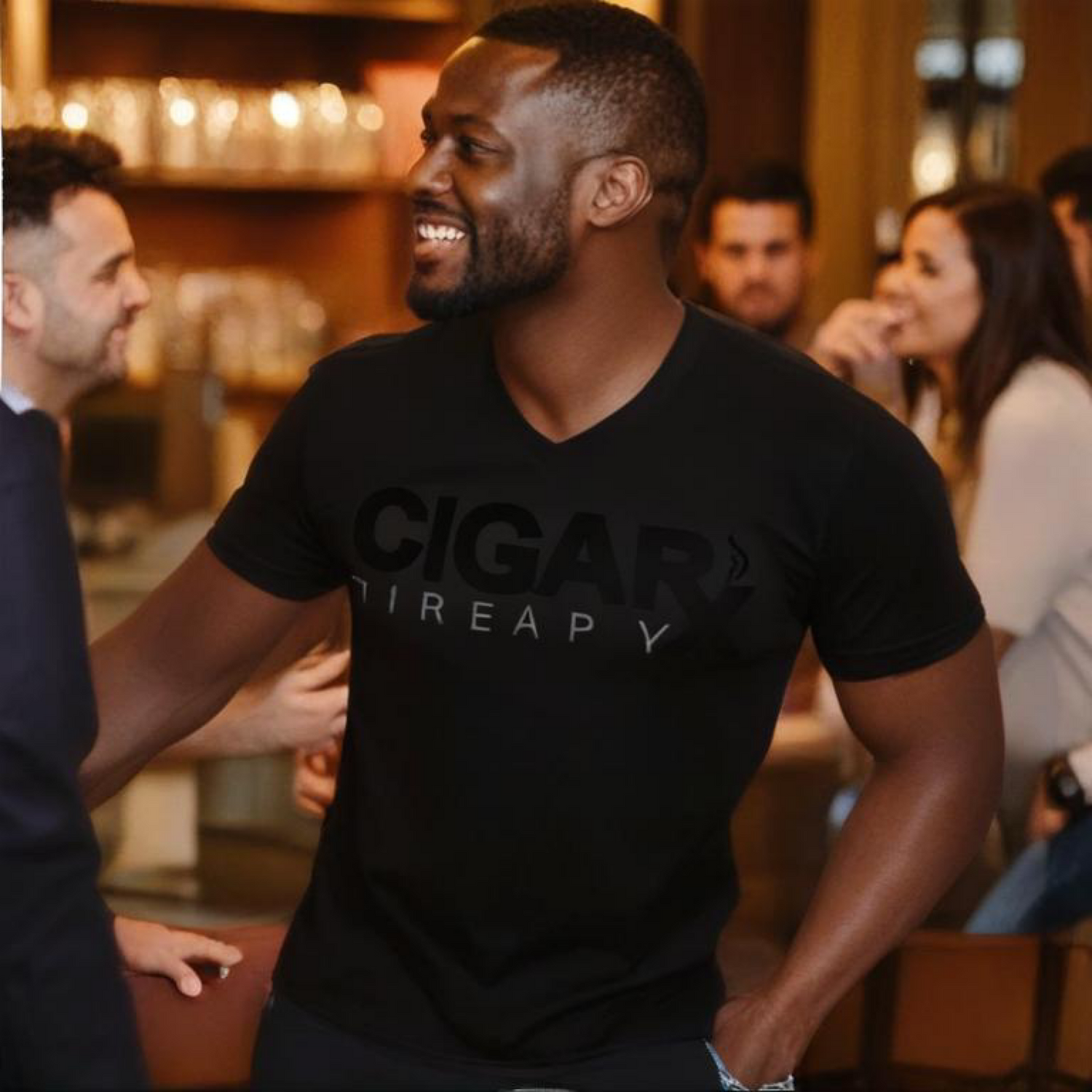 Man wearing a black 'Cigar Therapy' t-shirt in a social setting with people around